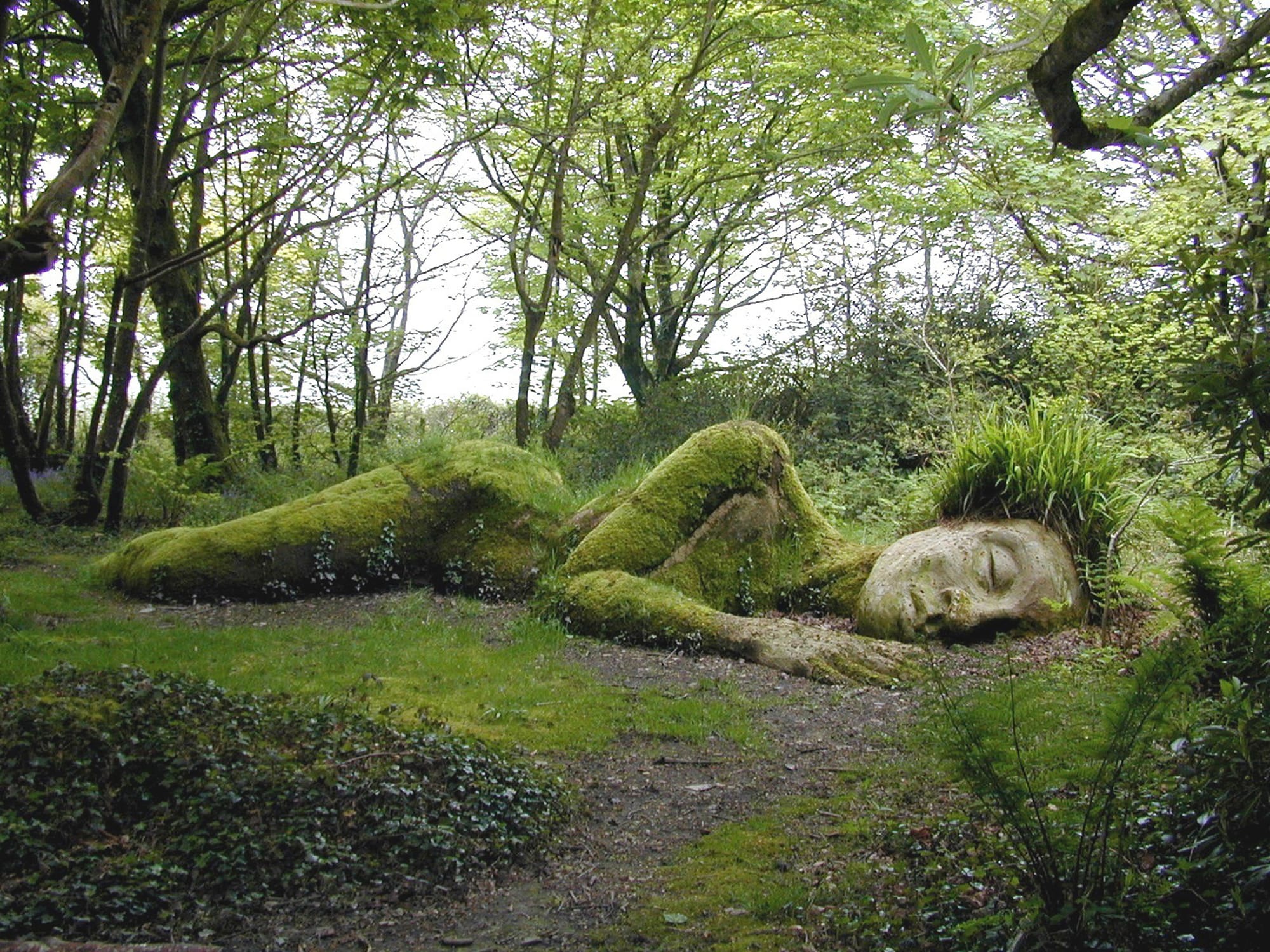 Sculpture of a stone person covered in moss in a woods.